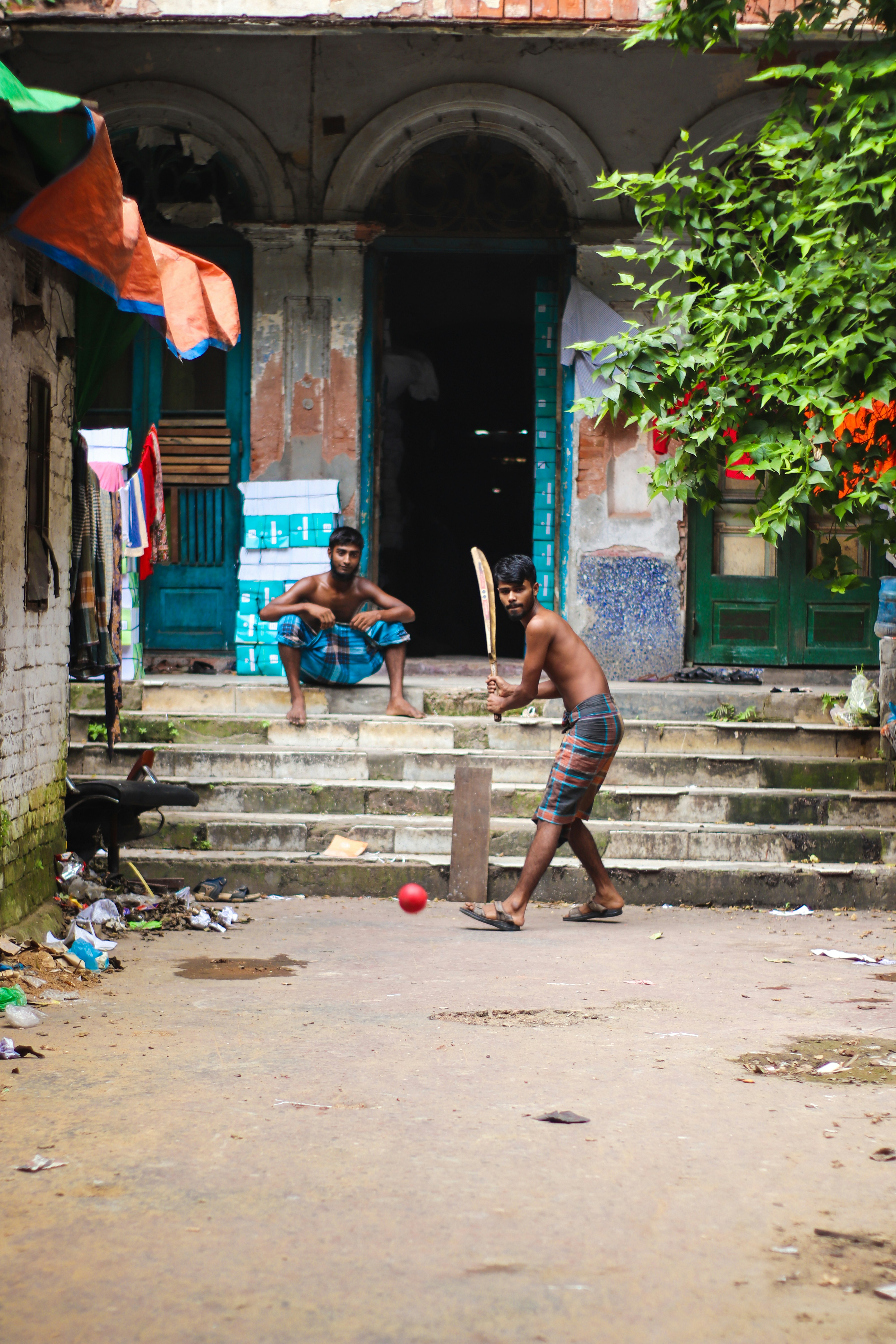 Barefoot street cricket outside an old house, played with a red ball